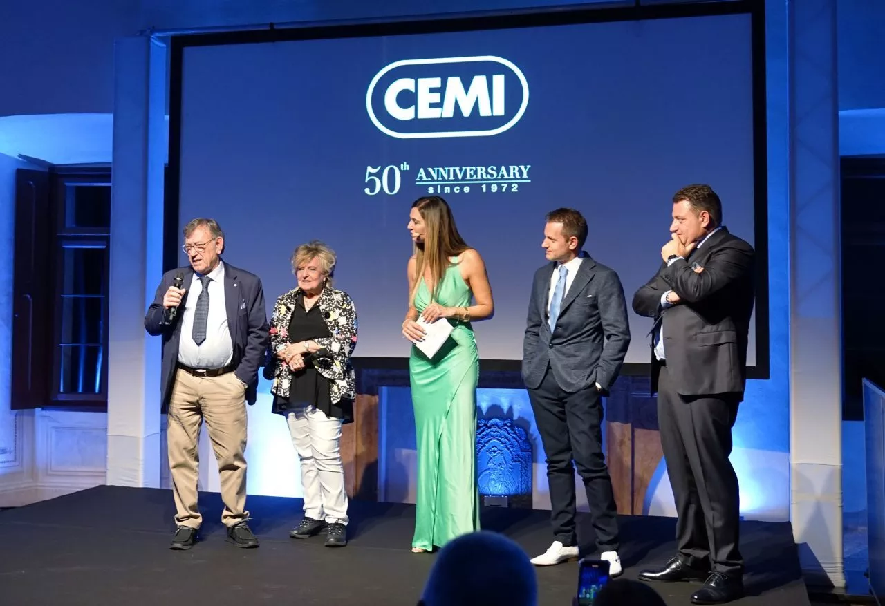 Un gruppo di cinque persone sul palco durante un evento che celebra il 50° anniversario del CEMI. Quattro sono in abiti formali, chiacchierano e sorridono, mentre uno tiene in mano un microfono. Alle loro spalle un grande schermo riporta il logo CEMI con la scritta "50° Anniversario dal 1972".