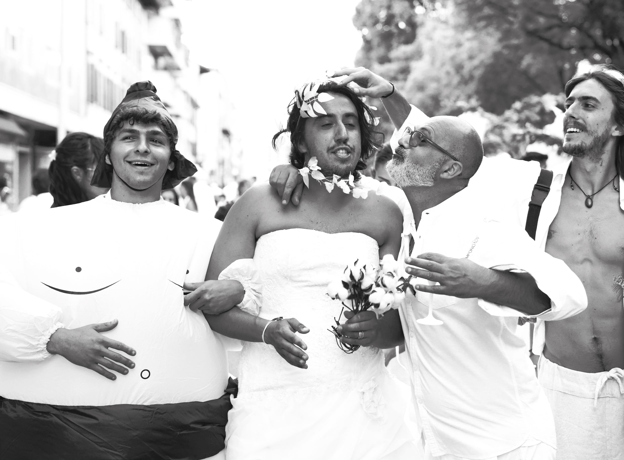 Un gruppo di uomini gioiosi partecipa a una parata; uno indossa un abito gonfiabile, un altro è vestito da sposa con un bouquet, mentre altri due, entrambi a torso nudo, ridono e interagiscono giocosamente con la "sposa", catturando l'estrosità generata dall'intelligenza artificiale.